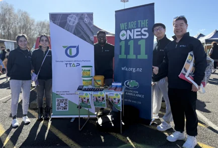 TTAP staff on a TTAP-branded stand at an outdoor community event, alongside a Wellington Free Ambulance display.