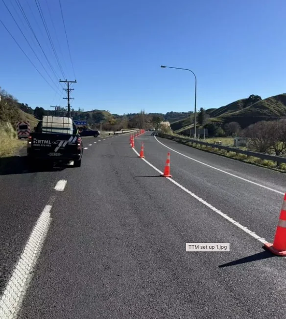 Temporary traffic management set up on a rural state highway — cones tapering the closed lane, a truck-mounted attenuator and a crew vehicle on the shoulder.