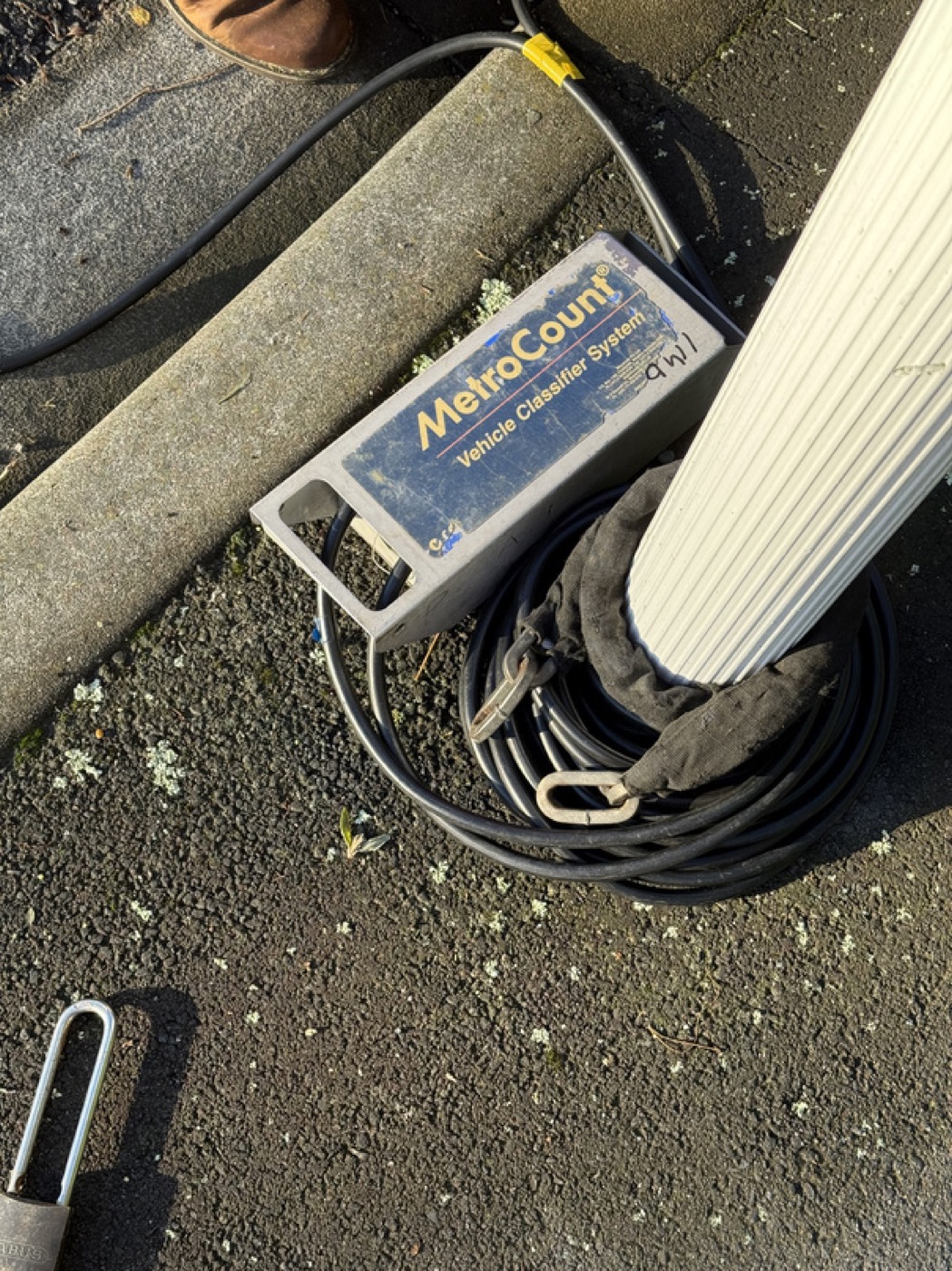 MetroCount Vehicle Classifier System (pneumatic tube traffic counter) sitting on New Zealand tarmac with cables coiled — typical TTAP field-deployed monitoring instrument.